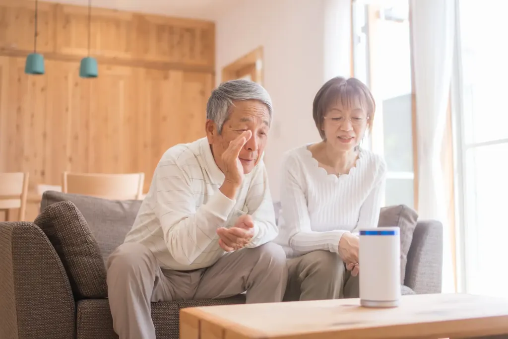 An elderly man engaging with a smart speaker alongside an elderly woman, illustrating the importance of technology in facilitating speech interaction.