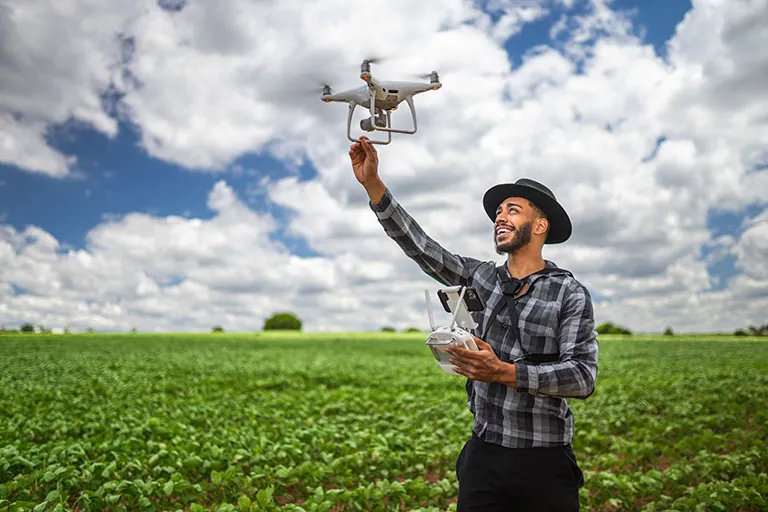A young farmer setting up a drone to monitor crop health, illustrating the use of modern technology in agriculture.