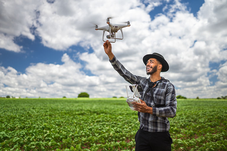A young farmer setting up a drone to monitor crop health, illustrating the use of modern technology in agriculture.