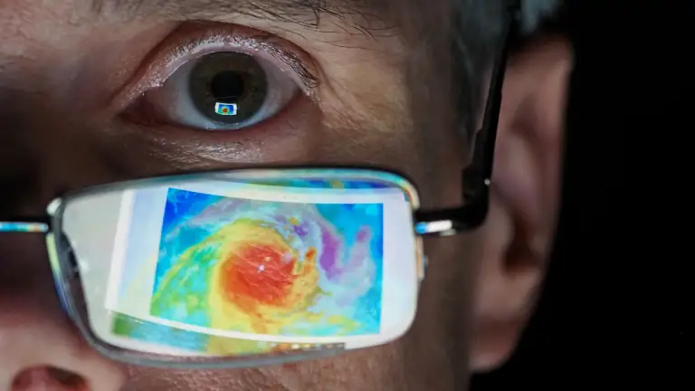 Meteorologist stares at impending hurricane with satellite image reflected on glasses. Concept image of the analysis work performed by concerned meteorologist looking at geospatial data.
